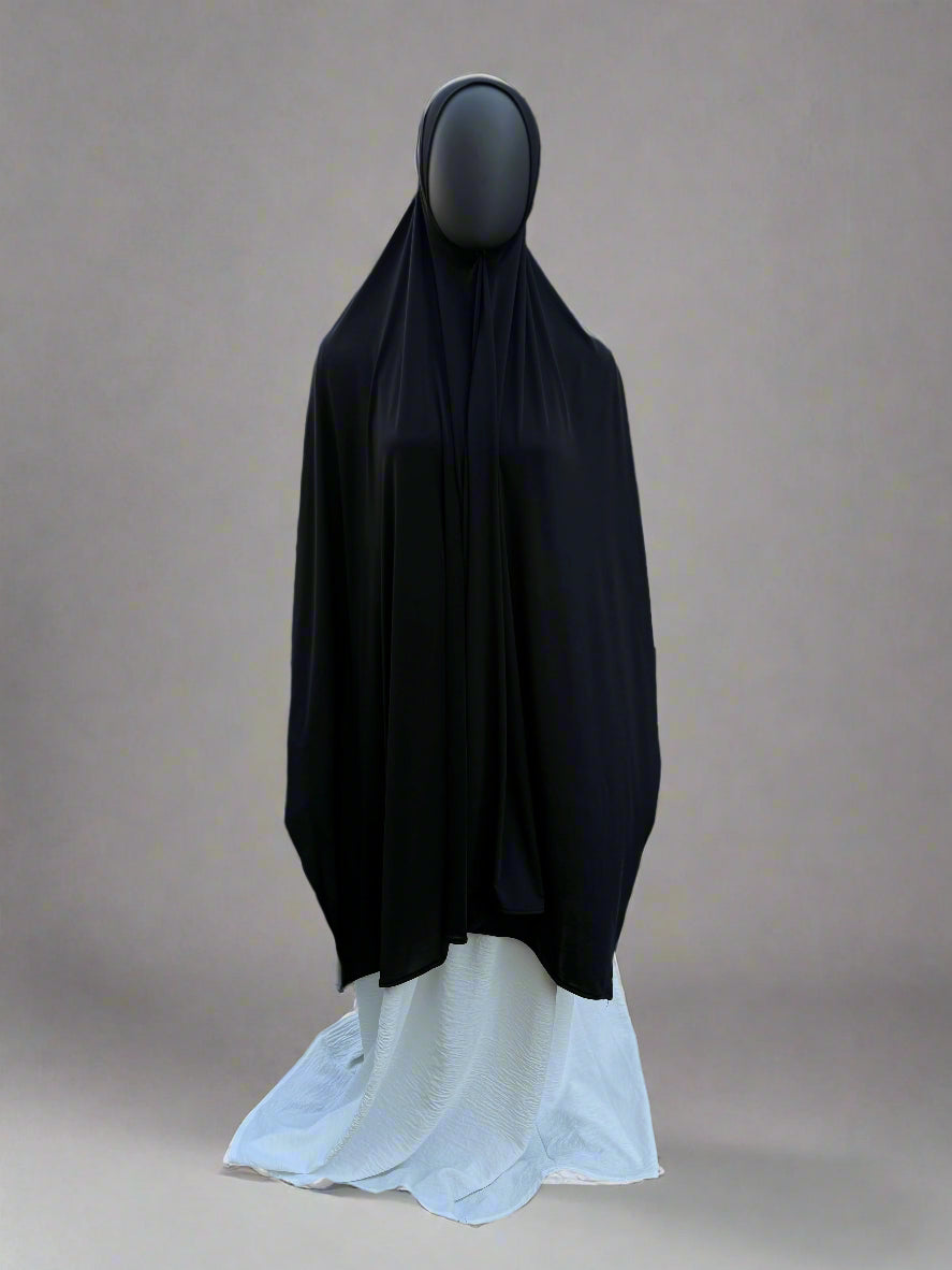 Mannequin wearing a black hijab and white dress in an outdoor setting.